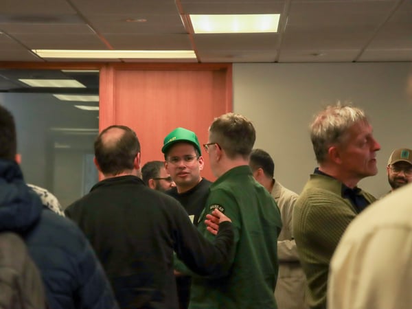A group of men are gathered in an indoor office setting, engaged in conversation.