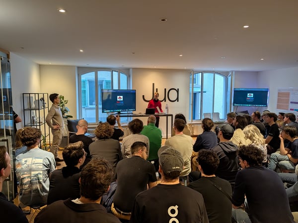 A group of people gathered in a modern office space for a presentation or product demo, with a presenter standing near a large screen.
