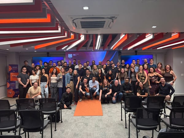 A large group of people posing for a group photograph in a modern indoor event space with distinctive orange and red ceiling panels.