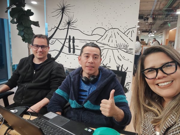 A group of three colleagues, two men and one woman, are posing for a friendly selfie in an office setting.