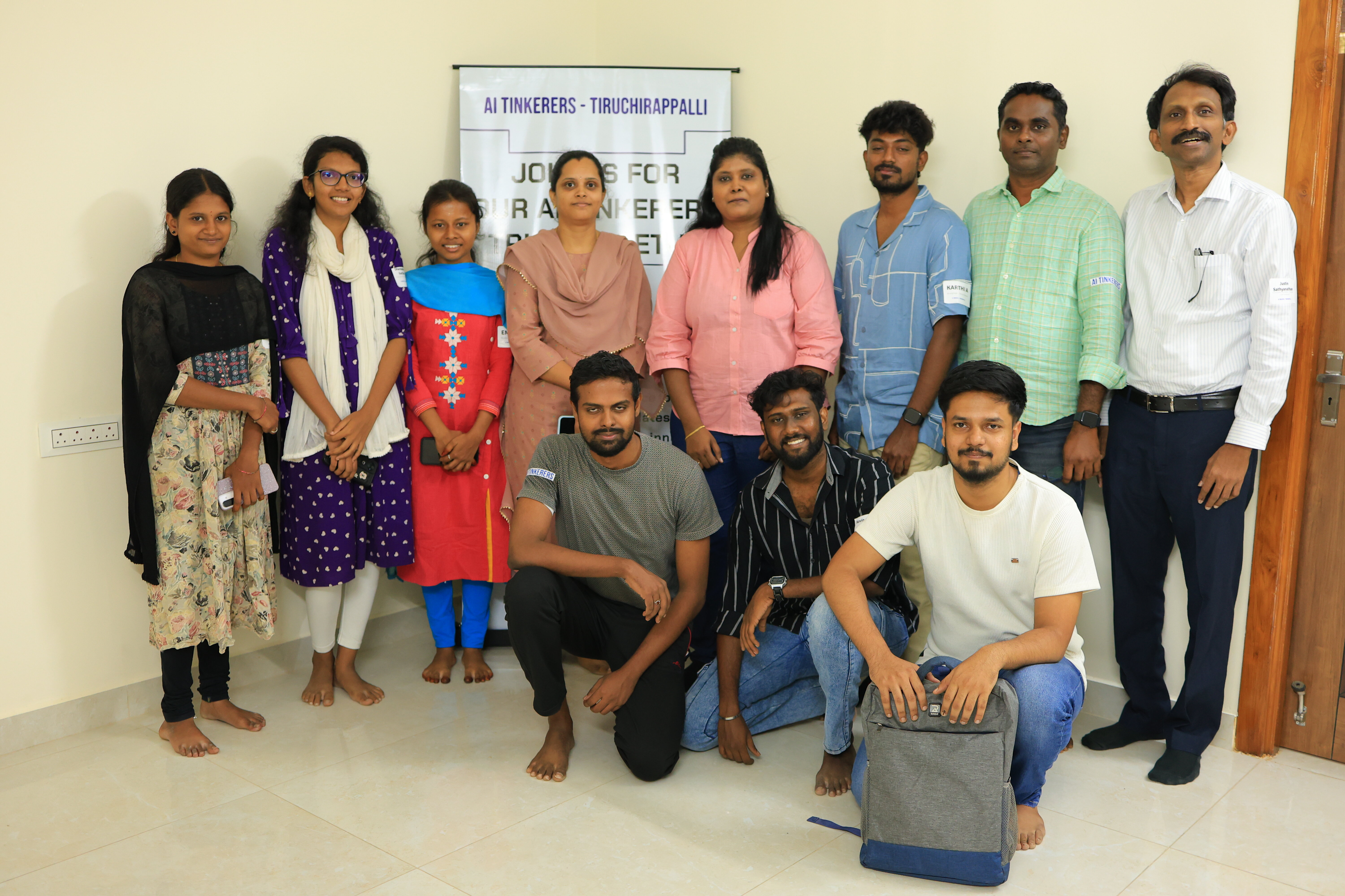 A group of eleven people, five women and six men, posing for a group photo indoors in front of an event banner.