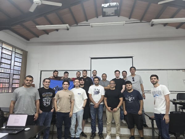 A group of seventeen men are posing for a group photograph in a classroom or meeting room environment.
