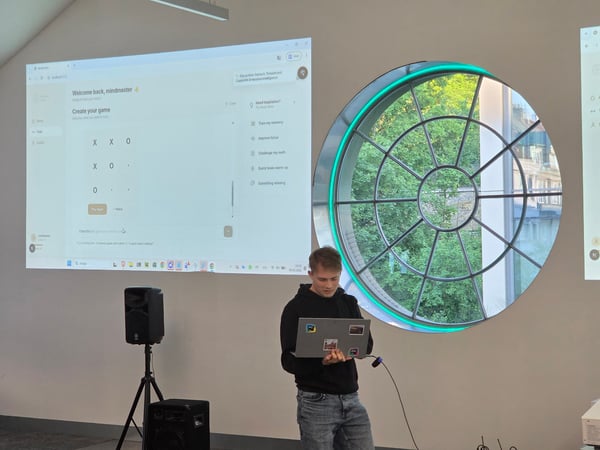 A man stands in a room holding a laptop while a screen behind him displays a projected interface for a brain-training game.