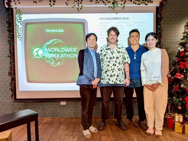 A group photograph shows four individuals standing in front of a large projection screen advertising the "ElevenLabs Worldwide Hackathon" event, set in an indoor space decorated with Christmas garlands and a Christmas tree.