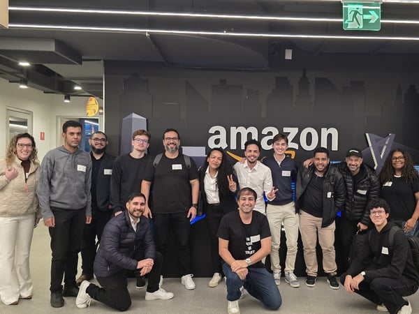 A group of colleagues posing together for a photo in front of a wall featuring the Amazon logo inside an office building.