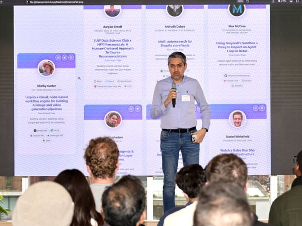 A man stands on a stage giving a presentation in front of a large screen displaying various project profiles and developer information to an audience.