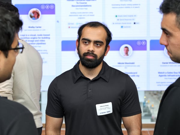 A man with a beard and a name tag stands in the center of a group, engaged in a conversation at a professional networking event.