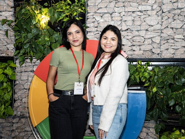 Two women posing for a photo in front of a decorative wall featuring plants, stones, and a large Google logo element.