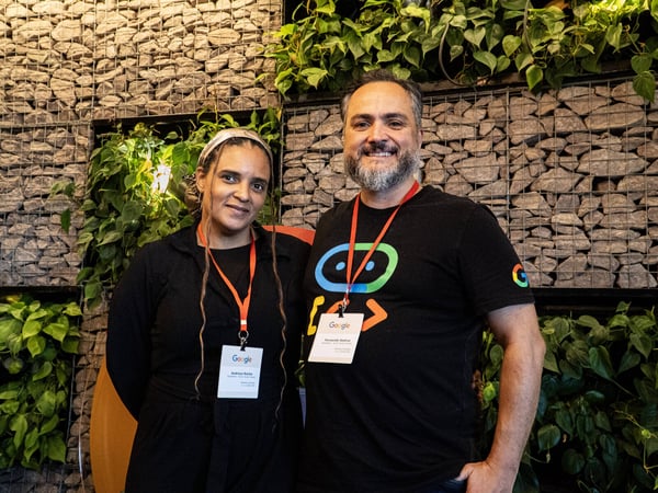 A man and a woman wearing Google-branded lanyards pose for a photo in front of a decorative wall made of stones and plants.