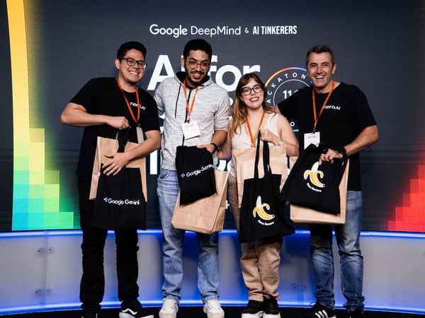 A group of four people stands on a stage in front of a Google DeepMind and AI Tinkerers backdrop, holding gift bags and tote bags.