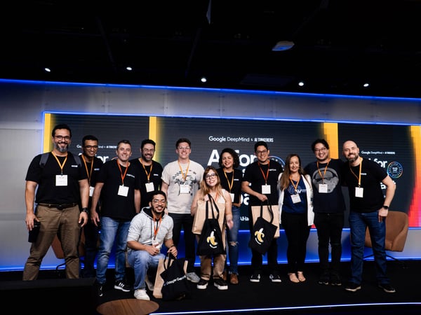 A group of twelve people posing for a photo on a stage in front of a screen displaying 'Google DeepMind & AI TINKERERS'.