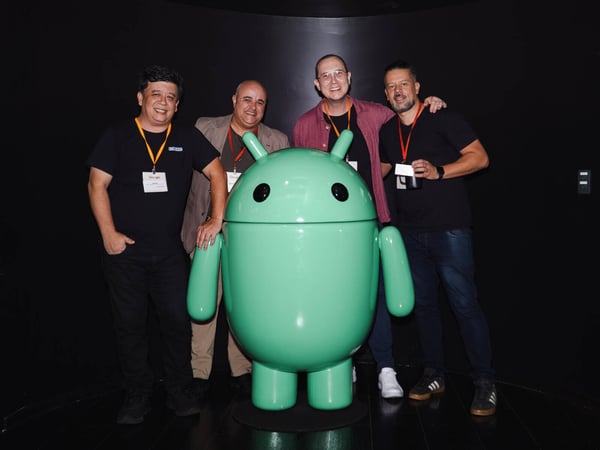 Four men are posing for a group photo alongside a large, green Android mascot statue in what appears to be a tech event setting.
