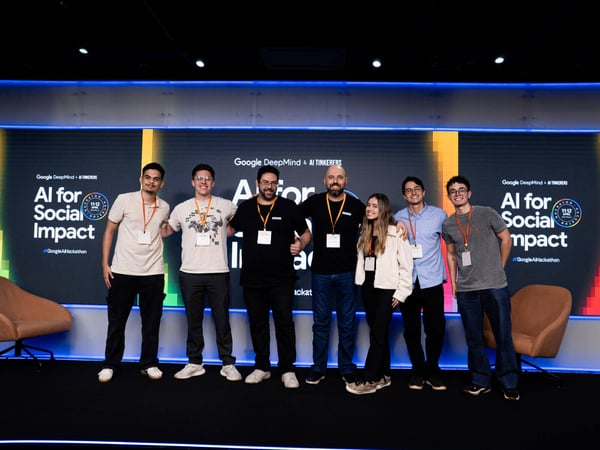 A group of seven people posing for a photo in front of a stage backdrop for a Google AI Hackathon event.