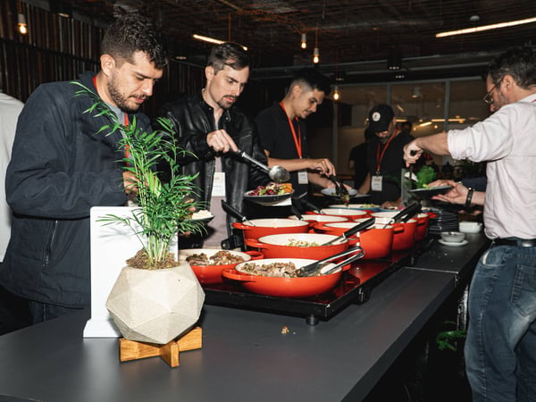 A group of people are serving themselves food from a buffet line featuring several bright orange pots.