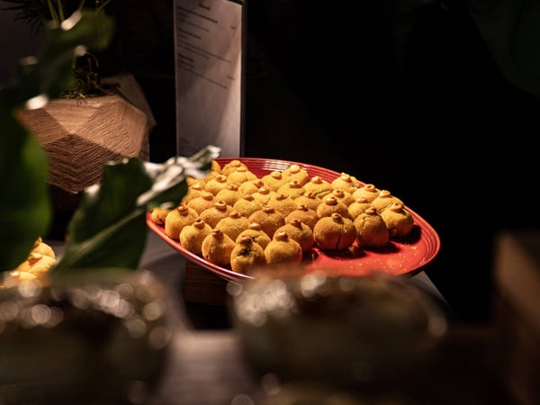 A close-up photograph of a red platter filled with small, golden-brown appetizers topped with a dollop of sauce, presented in a dimly lit indoor setting.