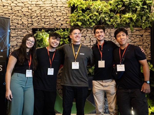 A group of five young adults, one woman and four men, posing for a photo in front of a stone and plant wall while wearing Google event badges.