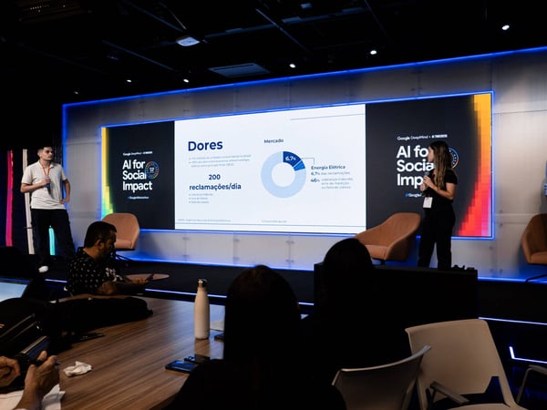 A woman stands on a stage giving a presentation about AI for Social Impact, with a large screen displaying data in Portuguese behind her.