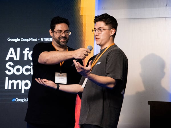 Two men are on a stage at a Google DeepMind event; one man holds a microphone for the other, who is speaking and gesturing with his hands.