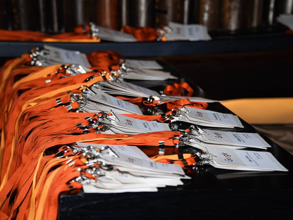 The image shows several stacks of event name badges with bright orange lanyards arranged on a dark surface, likely for event registration.