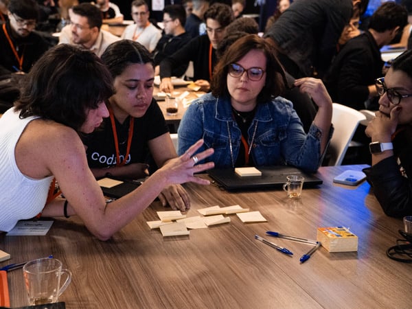 A group of people are gathered around a wooden table, engaged in a collaborative discussion using sticky notes and pens.