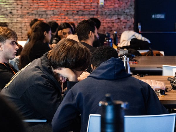 A group of people are seated at long tables in an indoor setting with a brick wall, appearing to be engaged in a workshop or collaborative session.