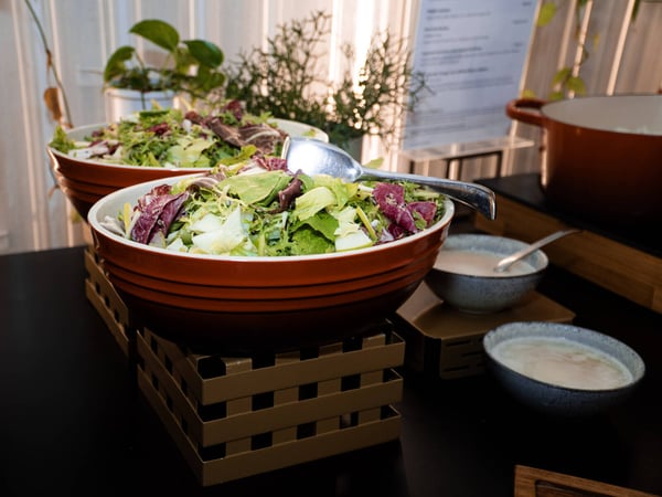 A buffet-style setup featuring large orange bowls of fresh mixed salad and small bowls of dressing on a dark table.