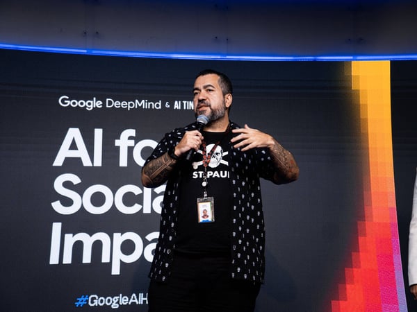 A man with tattoos and a beard is speaking into a microphone during a presentation for Google DeepMind.
