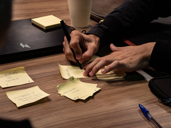 A close-up shot of a person's hands writing on yellow sticky notes during a brainstorming session on a wooden table.