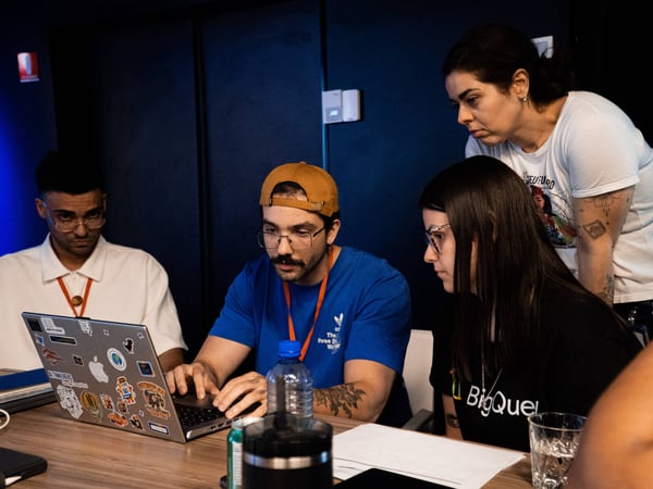 A group of four people are gathered around a laptop in a focused collaborative session, likely debugging or discussing a project.