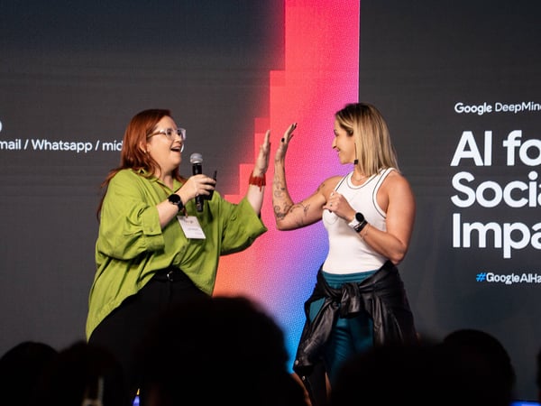 Two women on a stage give each other a high five during a Google DeepMind event titled 'AI for Social Impact'.