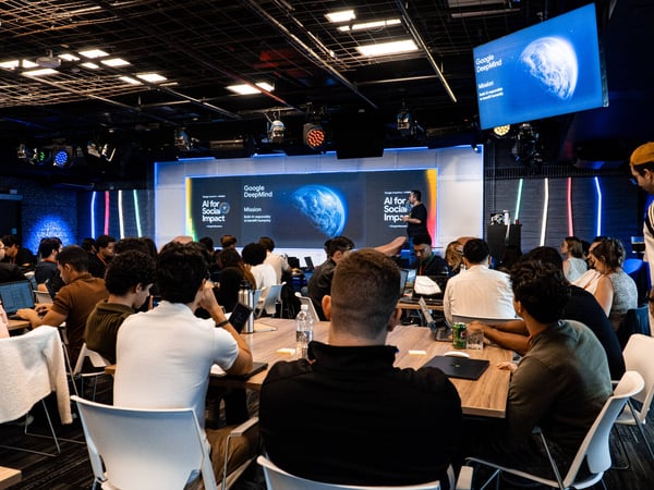 A group of people attending a Google DeepMind presentation titled 'AI for Social Impact' in a large, modern event space.