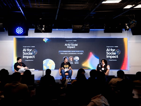 A photograph of a panel discussion titled 'AI for Social Impact' with three speakers on a stage in front of an audience.