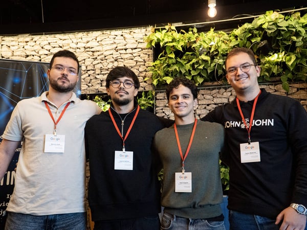 Four young men stand side-by-side posing for a group photo, each wearing a Google-branded lanyard and name tag.