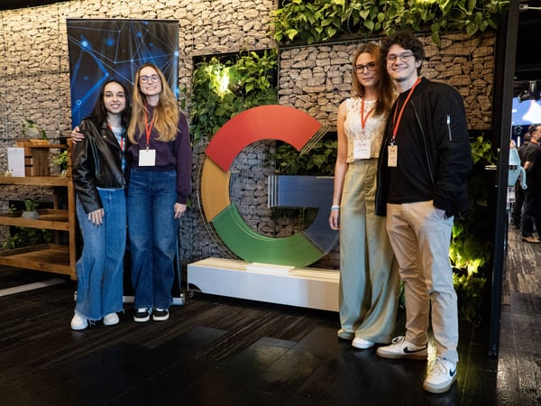 A group of four young adults posing for a photo next to a large, three-dimensional Google 'G' logo in a modern office or event space.