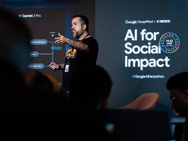 A man with tattoos is giving a presentation at a tech event titled 'AI for Social Impact', hosted by Google DeepMind and AI Tinkerers.