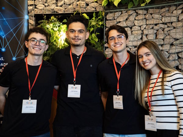 Four young people are smiling and posing for a group photo while wearing Google-branded lanyards and name badges.