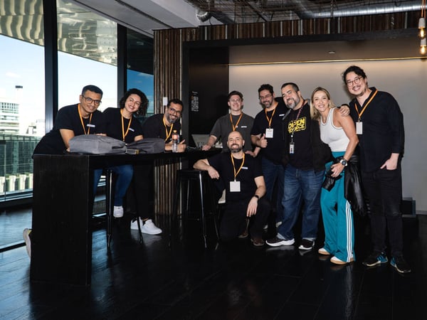 A group of nine people are smiling and posing for a photo in a modern indoor office or event space.