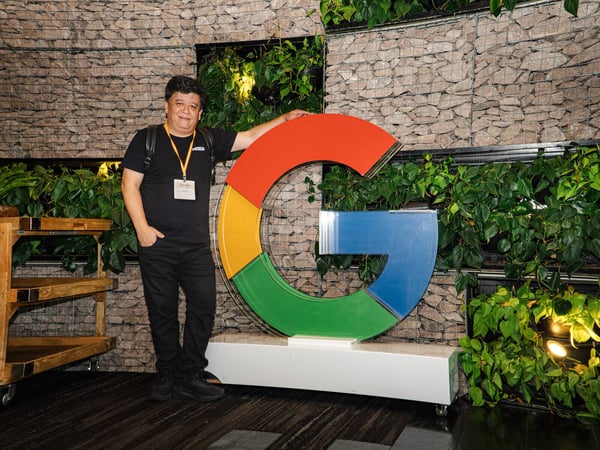 A man stands next to a large, three-dimensional Google 'G' logo against a backdrop of a stone wall with integrated plants.