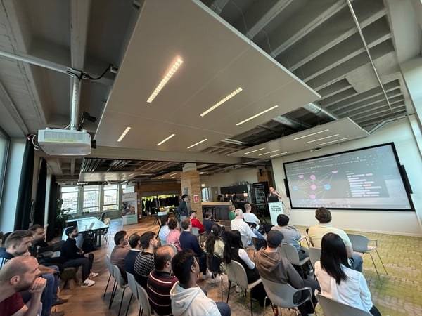 A group of people attending a technical presentation in a modern, industrial-style office space with a large projection screen.