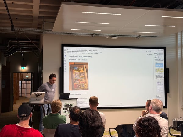 A man is giving a presentation about a 'Pokemon Card Scanner' to a small audience in a modern office or event space.