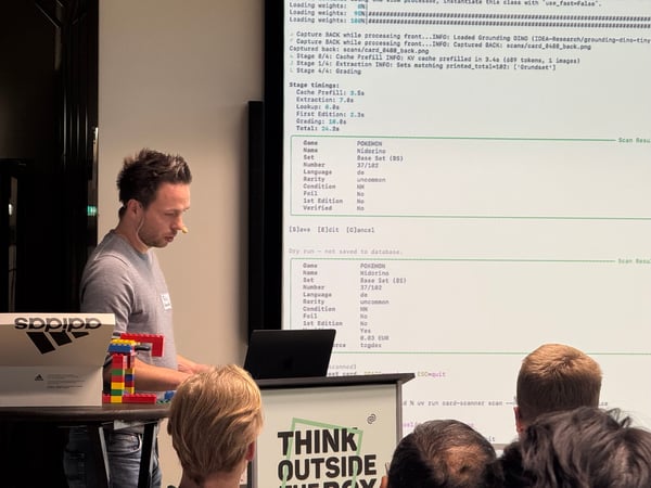 A man stands at a podium giving a technical presentation, with a large screen behind him displaying data from a Pokémon card scanner.
