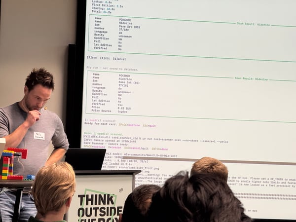 A man stands at a podium during a technical presentation, with a large screen behind him displaying data from a Pokémon card scanning application.