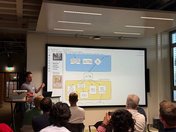 A man is giving a technical presentation in front of a large screen displaying a flowchart for an AI pipeline related to trading cards.