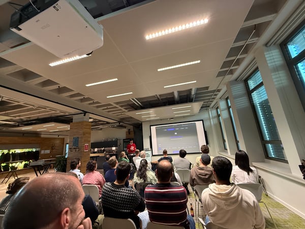A group of people are seated in a modern office space, watching a presentation displayed on a large screen.