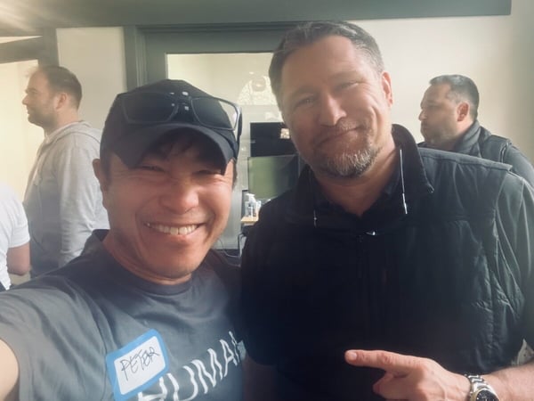 A selfie of two men smiling indoors, with one man wearing a name tag that says 'PETER' and the other pointing towards him.