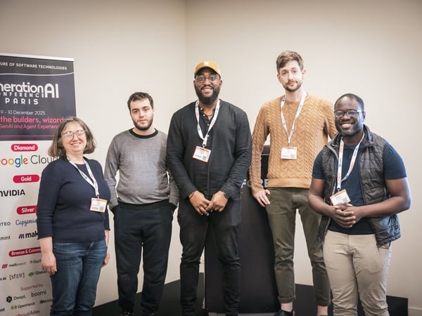 Five individuals (four men and one woman) wearing lanyards are posing for a group photo indoors, standing in front of a dark conference banner advertising the 'generation AI CONFERENCE PARIS'.