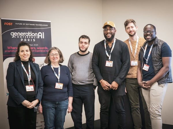 A group photograph shows six people (four men and two women) standing side-by-side indoors, smiling at the camera while wearing conference lanyards. Behind them is a black event banner advertising the 'generationAI CONFERENCE PARIS'.