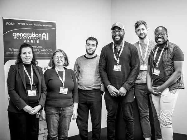 A black and white photograph captures a group of six conference attendees, consisting of four men and two women, standing together and smiling in front of a banner advertising the 'generationAI CONFERENCE PARIS'.