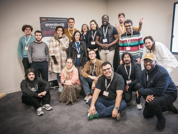 A group portrait of approximately 16 people, likely participants or staff of the "GenerationAI Conference," posing indoors in front of a promotional banner and a results screen.