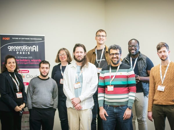 A group portrait of eight professionals, consisting of two women and six men, standing together indoors against a light wall, likely posing at a conference or event.